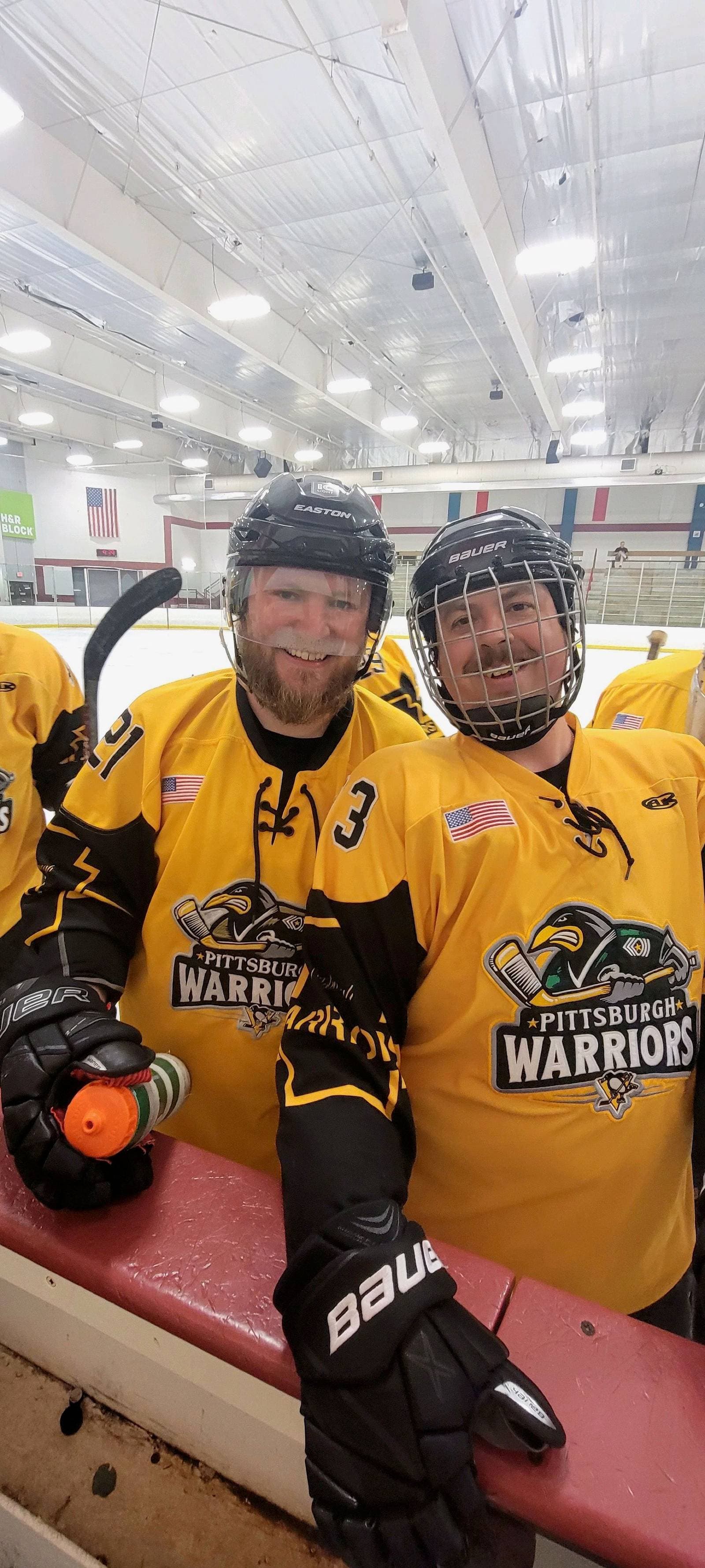 Two Pittsburgh Warriors players smiling on the bench after skating together.